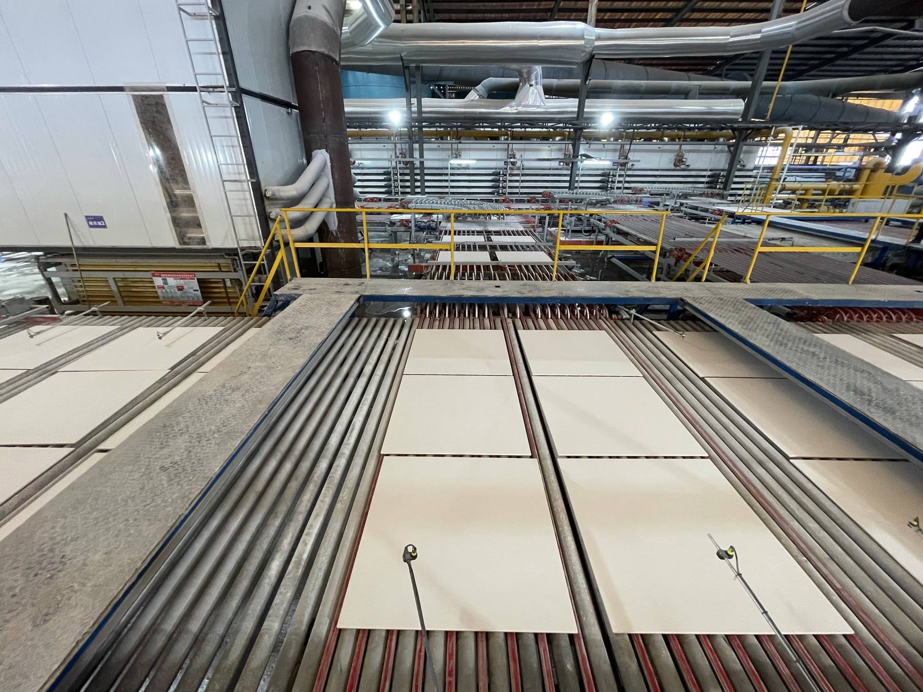 Large off-white tiles travelling on multi-lane roller conveyors under process heads